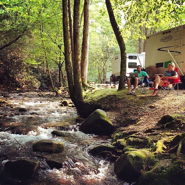 A couple relaxing in camp chairs on a river front site at Imagination Mountain Campground