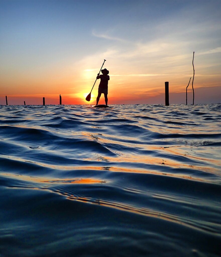 Woman standing on paddle board in bay at sunset